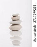 Simple zen-like composition featuring a balanced stack of stones on a white reflective surface, photographed in a studio setting. Perfect for themes around zen, mindfulness, or balance.