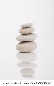 Simple zen-like composition featuring a balanced stack of stones on a white reflective surface, photographed in a studio setting. Perfect for themes around zen, mindfulness, or balance.