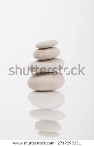 Simple zen-like composition featuring a balanced stack of stones on a white reflective surface, photographed in a studio setting. Perfect for themes around zen, mindfulness, or balance.