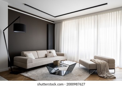 Simplicity and elegance in bright living room with big windows behind white curtains, big beige couch and seat, modern coffee table and black lamp