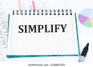 SIMPLIFY text on a notepad on an office desk next to marker, scores and charts