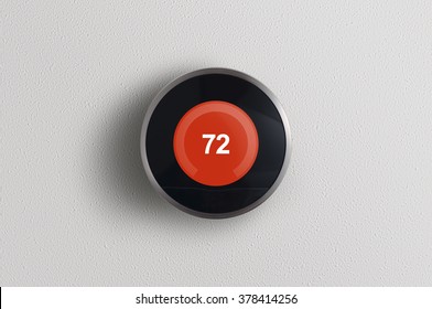 A Simplistic Photo Of A Round, Modern, Programmable Digital Thermostat, On A Clean White Wall In Heating Mode.