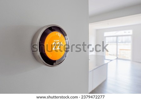 A simplistic photo of a round, modern, programmable digital thermostat, on a clean white wall in heating mode
