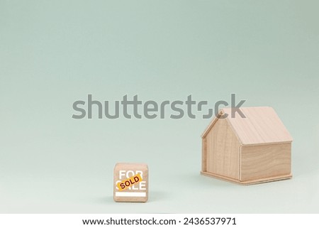 Simplistic wooden house model isolated on pale green background, with text SOLD on signboard.