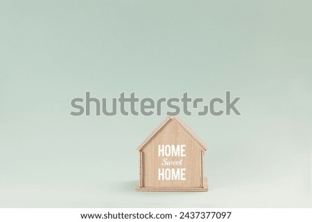 Simplistic wooden house model isolated on pale green background, with text Home Sweet Home on wall