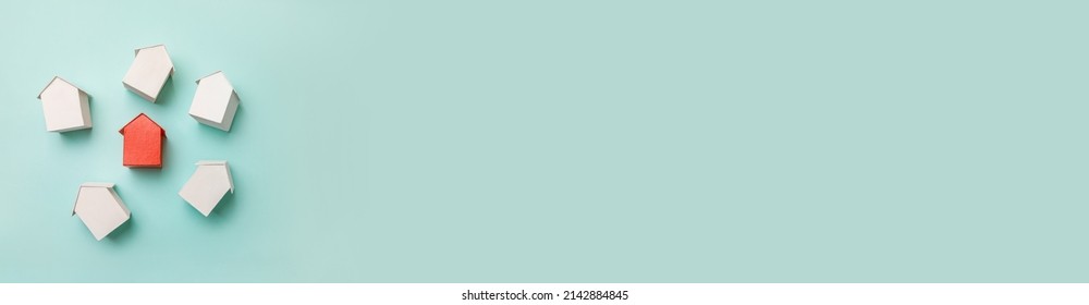Simply flat lay design with miniature red toy model house in among white houses isolated on pastel blue background. Real estate property industry. Community unique neighborhood choice concept. Banner