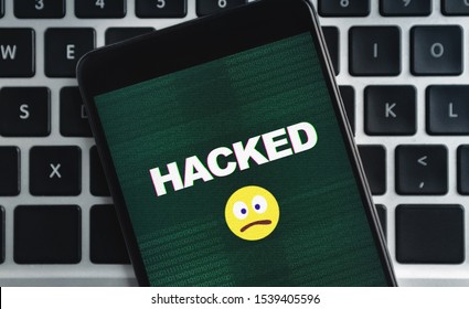 SIM-swap attack concept. Smartphone with hacked inscription and sad emoji icon on screen over laptop keyboard background - Shutterstock ID 1539405596