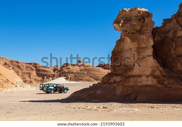 Sinai peninsula, Egypt -\
January 2022: Car in White Canyon in Sinai. Yellow and orange\
sandstone textured carved mountain, bright blue sky. Egyptian\
desert landscape