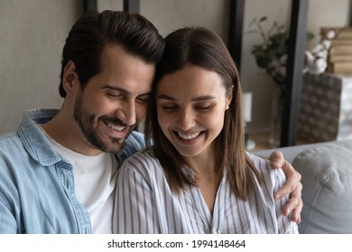 Sincere Affectionate Millennial Generation Couple Cuddling, Enjoying Peaceful Free Weekend Time Together, Sitting On Comfortable Sofa. Smiling Faces Of Romantic Loving Spouses Dreaming Indoors.