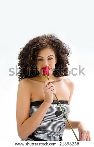 Sincere beautiful young woman with brown curly wild hair and bare shoulders smelling rose, isolated