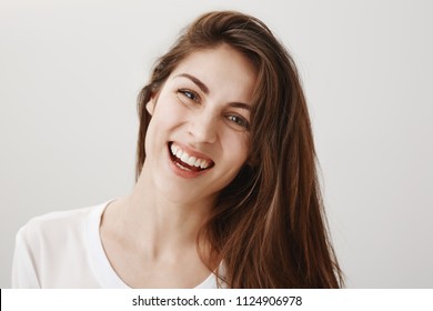 Sincere expression of joy. Portrait of attractive happy caucasian female coworker standing over gray background, tilting head and laughing out loud, being in great positive mood, hearing funny joke