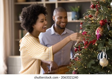 Sincere laughing happy mixed race family couple homeowners putting beautiful toys on evergreen festive tree, decorating interior preparing for merry Christmas or happy New Year winter holidays. - Powered by Shutterstock