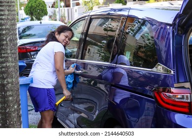 SINGAPORE - 10 APR 2022: A Happy Filipino Migrant Domestic Worker In Yio Chu Kang Estate Washes And Dries Her Employer's Car.