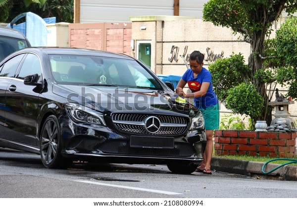 SINGAPORE - 15 JAN\
2022: A Foreign Domestic Worker in Lentor Estate is drying up her\
employer\'s car after washing it with shampoo and hosing it with\
water from the garden hose.\
