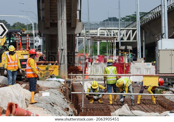 SINGAPORE - 15 OCT 2021: Migrant construction\
workers pour cement to build a new pavement in the Lentor Ave site\
of the North-South Corridor project.\
