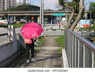 SINGAPORE - 16 APR 2021: A young lady uses an umbrella to shield from the harsh sunlight outdoors to avoid sunburn, skin cancer and freckle development during her walk along Yio Chu Kang road. 
