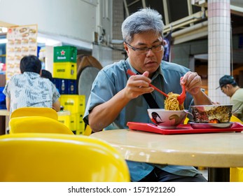 SINGAPORE - 17 MAR 2019 - A Middle Aged Asian Chinses Singaporean Man Enjoys A Late Night Bowl Of Noodles At An Eatery / Coffeeshop / Kopitiam / Hawker Centre.