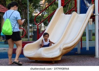 SINGAPORE - 25 MAY 2021: The Shy 14-month-old Boy Gains  Confidence When He Is Able To Slide Down By Himself. The Caring Filipino Foreign Domestic Worker Is Videoing His Achievement. 