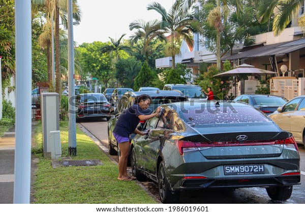 SINGAPORE - 4 JUN 2021: A foreign domestic worker (FDW)\
washes her employer\'s car. FDWs do general housework, cook, care\
for the family members with disabilities, the elderly and the \
younger. 