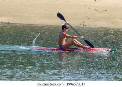 SINGAPORE - 9 JUN 2021: A novice kayaker, without wearing a personal floatation device, paddles in the shallow waters of Sentosa's Palawan beach. Kayakers in open seas should always wear life vests.