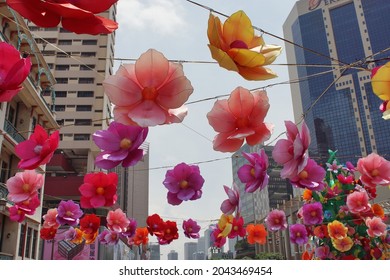 Singapore - Aug 2014: View Of Colorful Decorative Artificial Flowers Hanged Above Road During Festival Event With Building And Blue Sky Background. No People. 