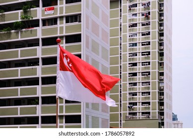 Singapore Flag Waving In The Wind Against Background Of HDB Flats. Selective Focus