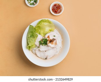 Singapore Food Sliced Fish Bee Hoon In A Bowl With Soup, Chili Sauce And Spring Onion Top View On Wooden Table