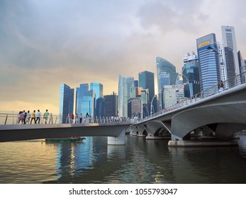 Singapore - January, 2018 : Group Of People Walking On The Bridge At Marina Bay Area, Is A Bay Located In The Central Area Of Finance And Business District Singapore In The Sunset Time.