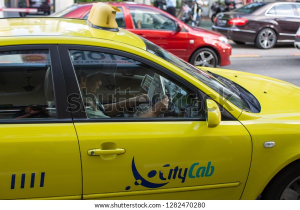 Singapore, January 7, 2019: Taxi driver reads\
the newspaper while in traffic stopped at a red light in the\
Kampong Glam district of\
Singapore