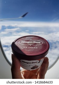 SINGAPORE - March 03 2019: Hand Holding Haagen Dazs Dessert Ice Cream In Airplane By Window With Blue Sky Above Ocean.