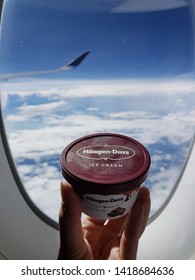 SINGAPORE - March 03 2019: Hand Holding Haagen Dazs Dessert Ice Cream In Airplane By Window With Blue Sky Above Ocean.