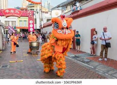 Singapore - March 24, 2018: People in traditional costume perform the Chinese lion dance while others play musical instruments and onlookers watch, Chinatown