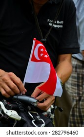 Singapore - May 1, 2013: A Protester Steadies A Singapore Flag On His Bicycle At May Day Rally In Singapore Speakers Corner Held To Protest  Immigration Policies To Increase Singapore's Population. 