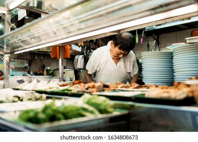 Singapore, Oct 2019: Old Man In Apron Preparing And Cooking Traditional Chinese Food At Street Food Stall At A Hawker Centre. Asian Cuisine