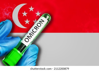 Singapore Outbreak Of Omicron Variant. A Hand In A Blue Rubber Glove Holds A Test Tube With Covid-19 Virus Omicron In Front Of Singapore Flag. Omicron Variant Outbreak Concept