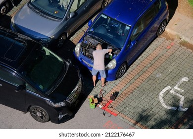 Singapore Sep2021 High Angle Of Man Fixing Engine Of Blue Car Parked At HDB Neighbourhood Carpark, Next To Wheelchair Parking Lot.