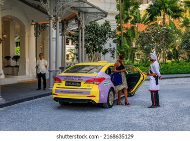 Singapore - September 08, 2019: Black Woman Stepping Out Of A Taxi At The Iconic Raffles Hotel, Assisted By Staff Sikh Doorman In A Military Uniform