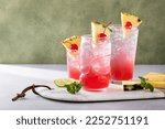 Singapore sling cocktail in variety of glasses garnished with pineapple and cherry with copy space