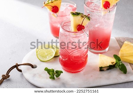 Singapore sling cocktail in variety of glasses garnished with pineapple and cherry
