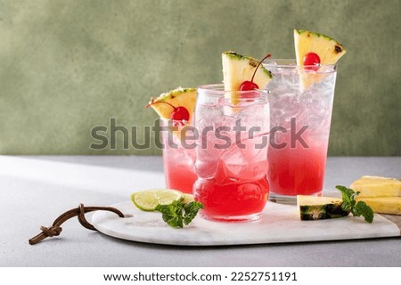 Singapore sling cocktail in variety of glasses garnished with pineapple and cherry with copy space