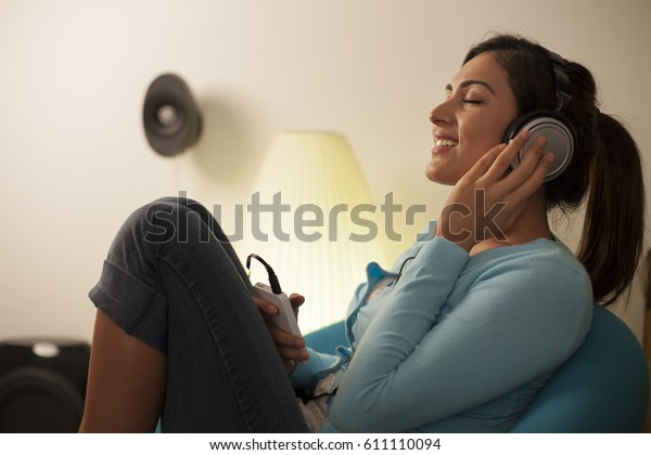 Singapore,\
Young woman listening to music in living\
room