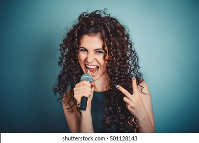 Singer. Closeup Head Shot Sexy Beautiful Happy Young Woman Lady Girl Singing With Microphone Showing Peace Two Sign Gesture Blue Background. Positive Human Emotion Expression Feeling Life Perception 