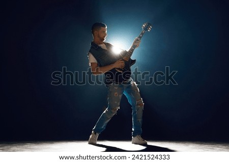Singer with electric guitar jumping in moment on stage. Vocalist performing with spotlights behind him. Concept of Rock-n-roll, music and dance, festivals and concerts, culture.