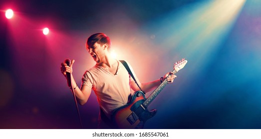 Singer with a guitar and microphone on the stage in stage lighting - Powered by Shutterstock