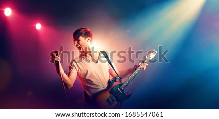 Singer with a guitar and microphone on the stage in stage lighting