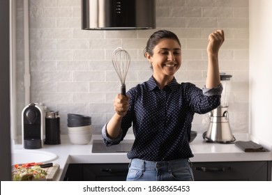 Singer In Heart. Enthusiastic Young Indian Woman Enjoy Preparing Food At Modern Home Kitchen. Funny Young Hindu Female Take Break In Cooking Listen To Music Dance Sing With Microphone Of Egg Beater