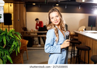 Singer, host of events in a blue dress with a microphone in the interior of the restaurant. MINSK, BELARUS, June 15, 2022