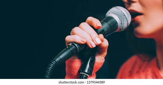 Singer at microphone. Woman singing and holding mic. Female vocal talent. Music show recital.