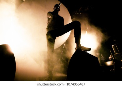 A Singer is on the stage. A silhouette of the singer is putting his foot on a speaker. A brutal shadow of a rapper on the stage. Smoke and bright soft yellow stage lights in the background. - Powered by Shutterstock