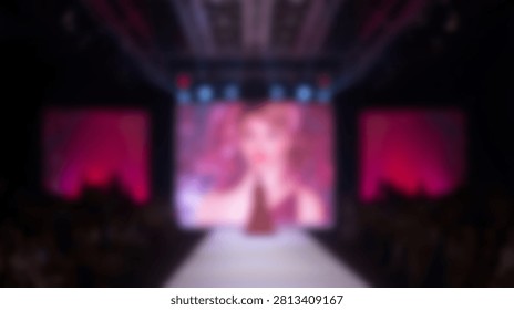 A singer is performing live on a stage with a large screen behind them displaying a colorful image, illuminated by spotlights.